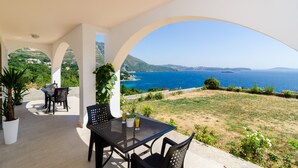 A covered patio with a table and chairs, overlooking a coastal landscape with clear blue sea and distant hills. - Apartments A&M - Studio with Terrace and Sea View No. 2 (Mlini)