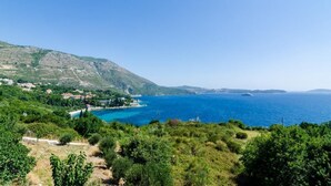A coastal landscape with a clear view of the sea, a small island, and a hillside with buildings.