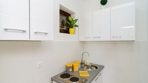 A compact kitchen with white cabinets, a small window with a plant, a sink, and a stove.
