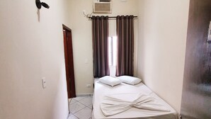 Una habitación pequeña y limpia con una cama, un ventilador de techo y un aire acondicionado, además de una puerta.