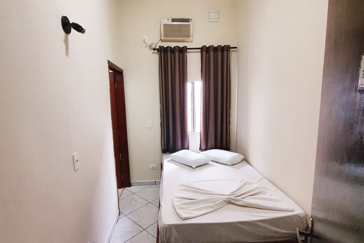 A small, clean room with a bed, a ceiling fan, an air conditioning unit, and a door.