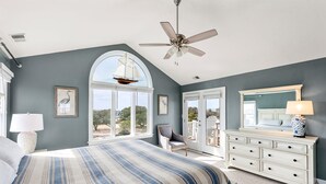 Ein Schlafzimmer mit einem großen Bett, einem Deckenventilator, einem Schminktisch und einem Fenster mit Blick auf ein Segelboot.