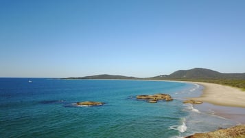 Enjoy the serene coastal landscape with a sandy beach, rocky outcrops, and a hilly backdrop.
