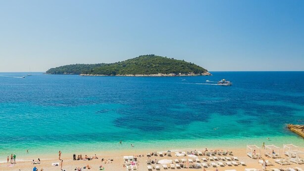 Una playa con agua turquesa cristalina, una orilla arenosa y una pequeña isla a lo lejos.