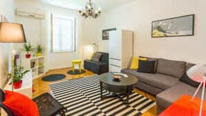 Una sala de estar moderna con sofá, mesa de centro, lámpara, estantería y un cuadro en la pared.