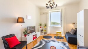 Un espacio habitable compacto con sofá, mesa de comedor, televisor y ventana con vista a una colina.
