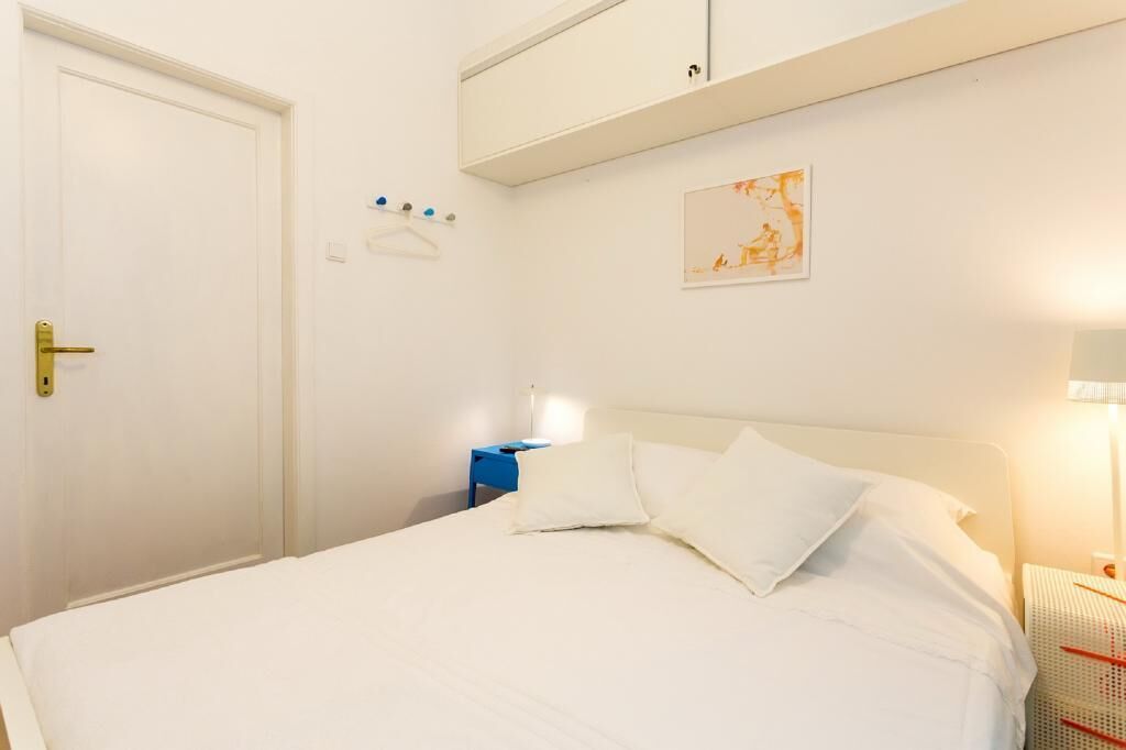 Een keurig ingerichte hotelkamer met een bed, nachtkastje, wandplank en een deur.
