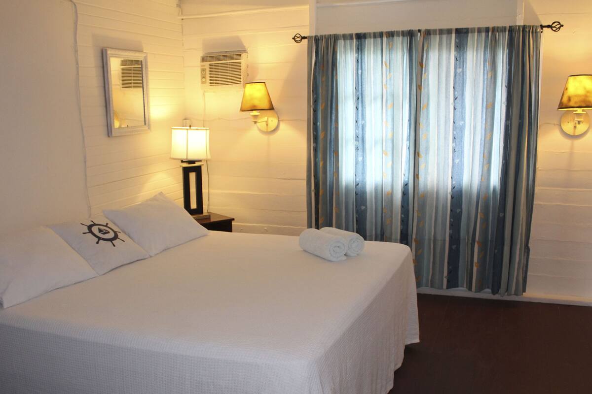 A neatly made bed with pillows, a bedside lamp, and a rolled towel on the nightstand.