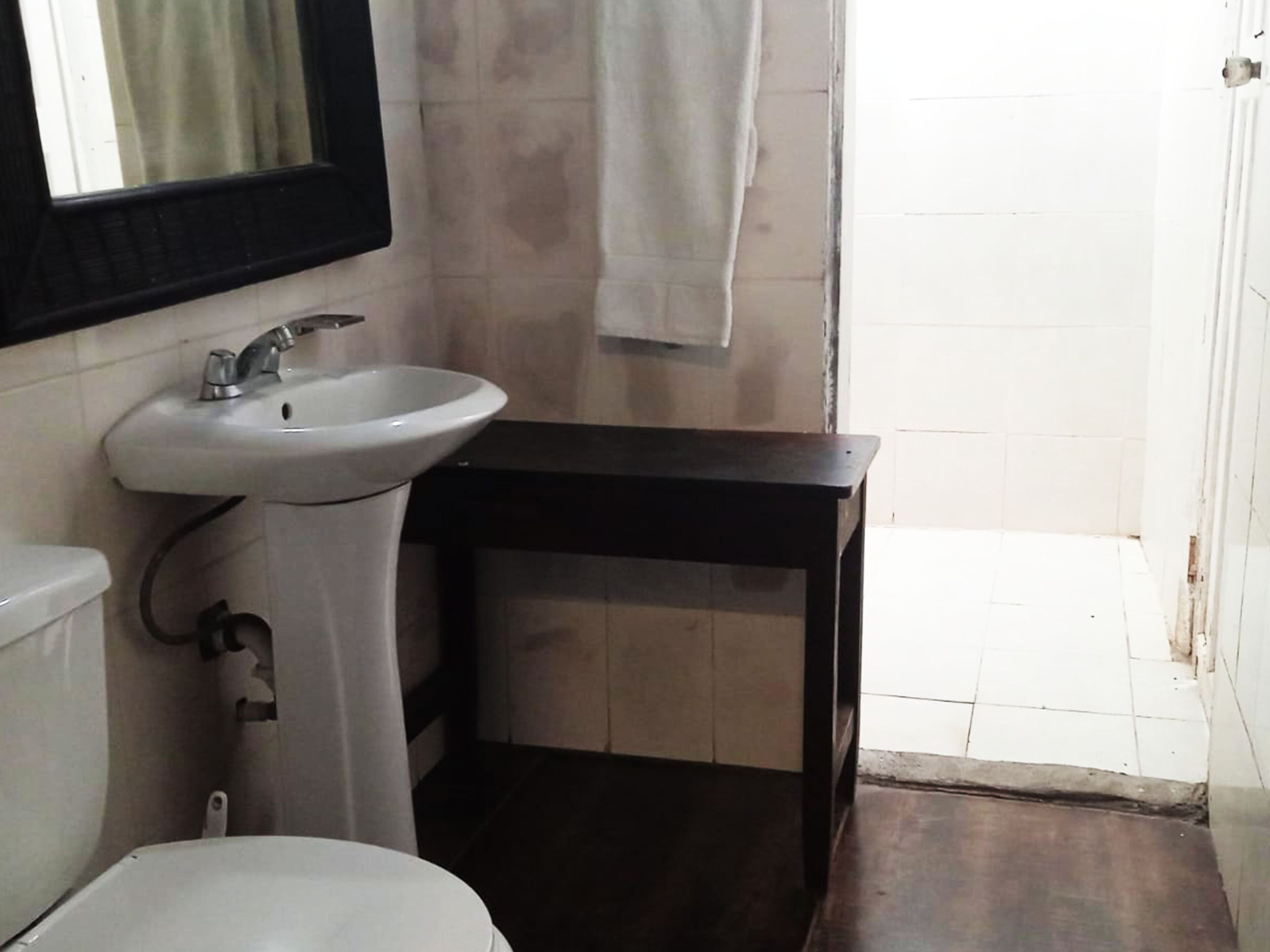 Un baño con un lavabo blanco, un espejo y una mesita de madera oscura.