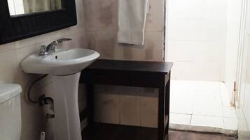 Un baño con un lavabo blanco, un espejo y una mesita de madera oscura.