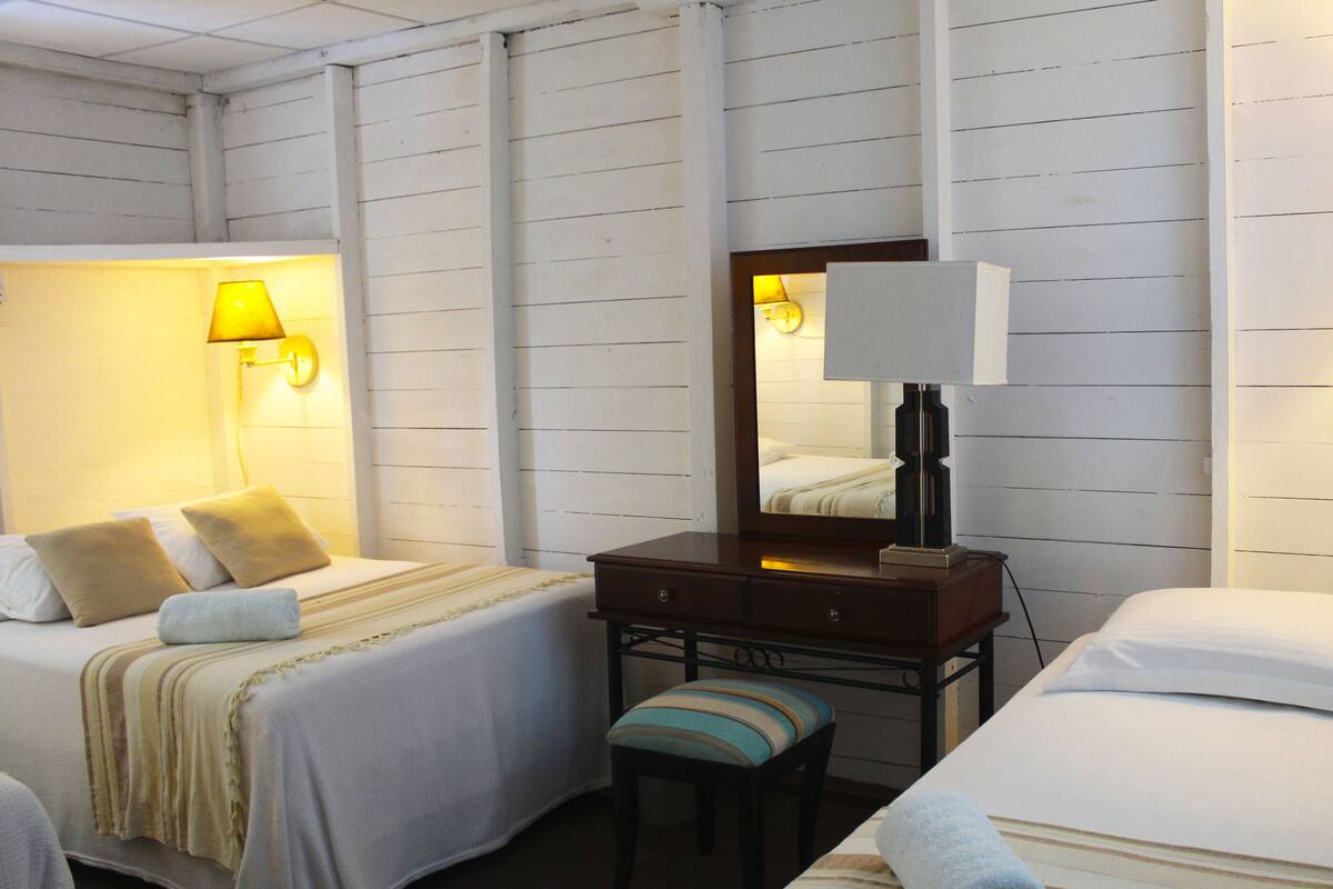 A hotel room with two beds, a nightstand, a mirror, and two wall-mounted lamps.