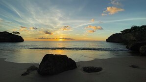 A beach with a sunset, calm sea, and rocky outcrops. - Sol Patch at Jeremi #2: a seaside guest house overlooking the Caribbean. (Willemstad)