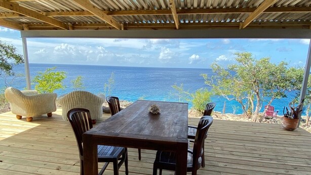 A wooden deck with a table and chairs, overlooking a beach and ocean. - Sol Patch at Jeremi #2: a seaside guest house overlooking the Caribbean. (Willemstad)