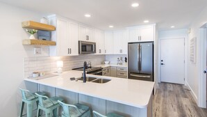Una cocina moderna con armarios blancos, un refrigerador de acero inoxidable y una barra con cuatro taburetes.