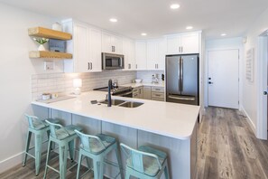 A modern kitchen with white cabinets, a stainless steel refrigerator, and a bar area with four stools. - Lovely GULF FRONT unit with amazing Beach Views from the balconies of LR and MB! (Santa Rosa Beach)