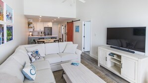 Una sala de estar moderna con un sofá blanco, una mesa de centro y un televisor sobre un mueble de madera.