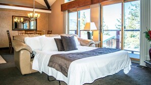 A spacious bedroom with a large bed, a chandelier, a dining table, and a view of the outdoors through large windows. - Charming 2-bedroom townhome in Incline Village close to mountain and restaurants (incline village)