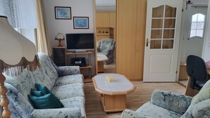 Una sala de estar con sofá, sillones, una mesa de centro, televisor y armario.