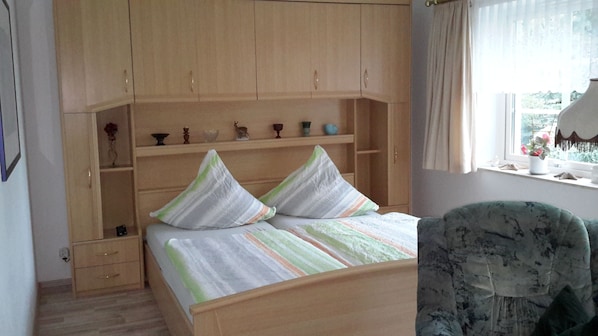 Ein Schlafzimmer mit einem Bett, einem Stuhl, einem Fenster und einem Regal mit Dekorationen.