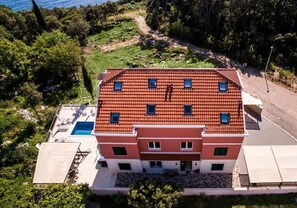 Un immeuble à plusieurs étages, doté d’un toit recouvert de tuiles rouges, d’une piscine et d’une allée pavée.