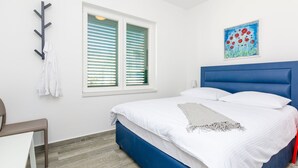 Een slaapkamer met een bed, een stoel, een kapstok, een raam met jaloezieën en een schilderij aan de muur.