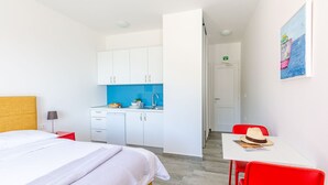 Habitación de hotel con cama, una kitchenette pequeña, una mesa de comedor con una silla roja y un cuadro en la pared.