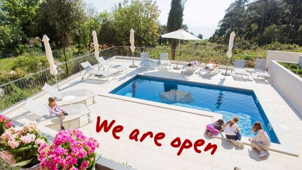 Zona de piscina con sillones de descanso y un cartel que dice 'Abierto'.