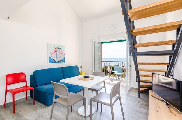 Un salon moderne avec un canapé bleu, un fauteuil rouge, une table blanche et un téléviseur.