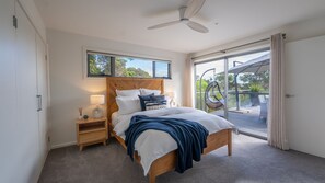 Ein Schlafzimmer mit Bett, Nachttischen, Deckenventilator und Blick ins Freie durch eine Schiebetür.