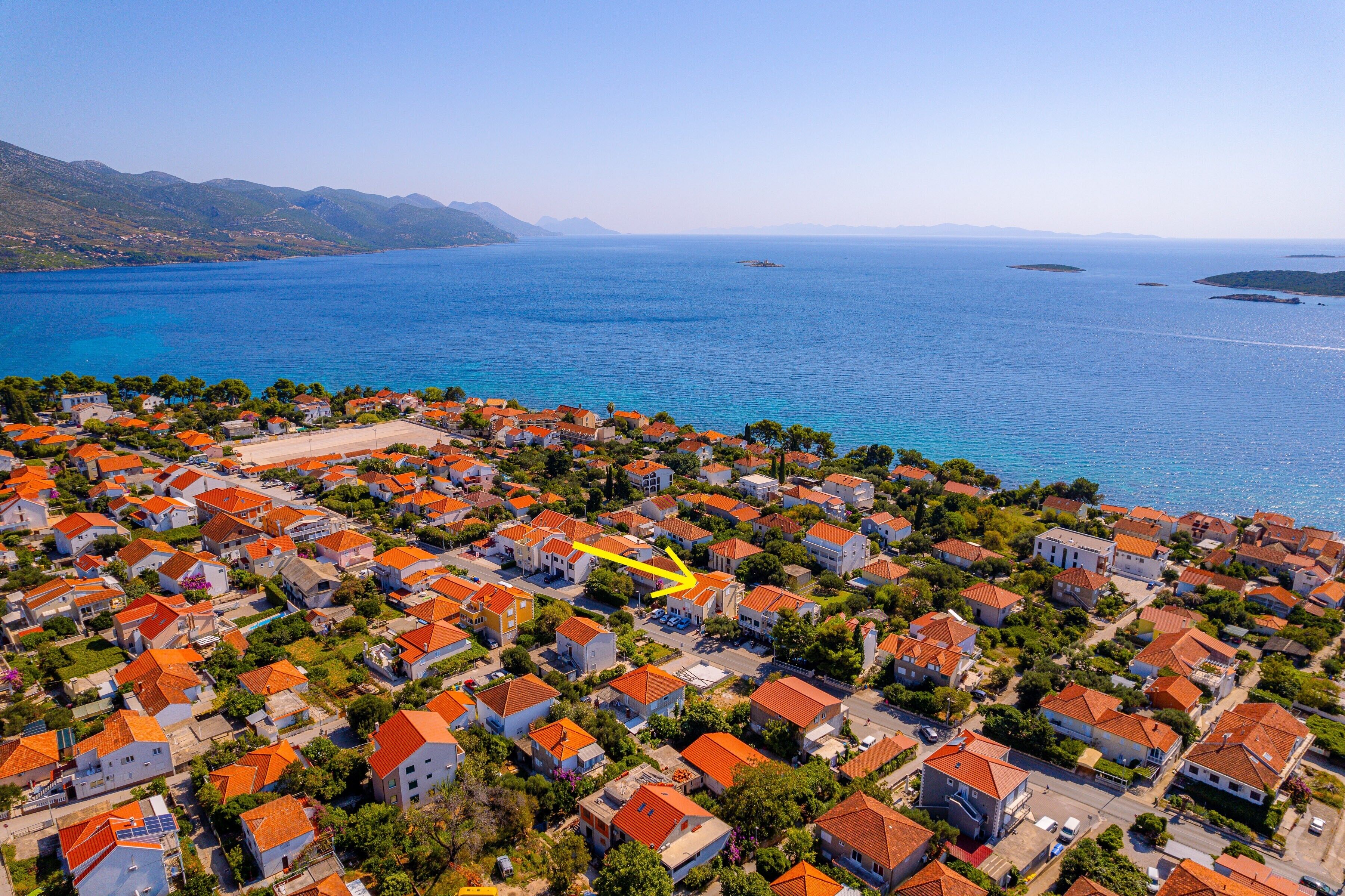 An aerial view of a coastal residential area with houses, a beach, and a clear blue sea.