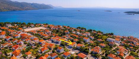 An aerial view of a coastal residential area with houses, a beach, and a clear blue sea.