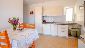 A compact kitchen with white cabinets, a dining table with a white tablecloth, and a vase of flowers. - Apartments Mladenka- Two Bedroom Apartment with Balcony and Sea View (Orebic)