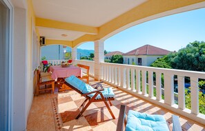 Un balcon avec une table et des chaises, un fauteuil confortable et un point de vue sur les maisons et la verdure.