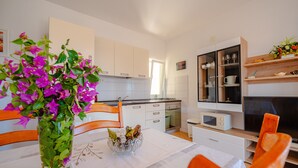 A modern kitchen with white cabinets, a dining table with orange chairs, and a vase with purple flowers. - Apartments Mladenka- Two Bedroom Apartment with Balcony and Sea View (Orebic)