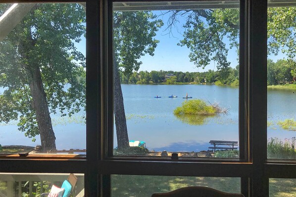 Vista de un lago desde una ventana, con un banco y una mesa de picnic en el exterior.