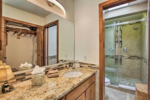 Un baño con encimera de granito, lavamanos, espejo, ducha y tocador de madera.