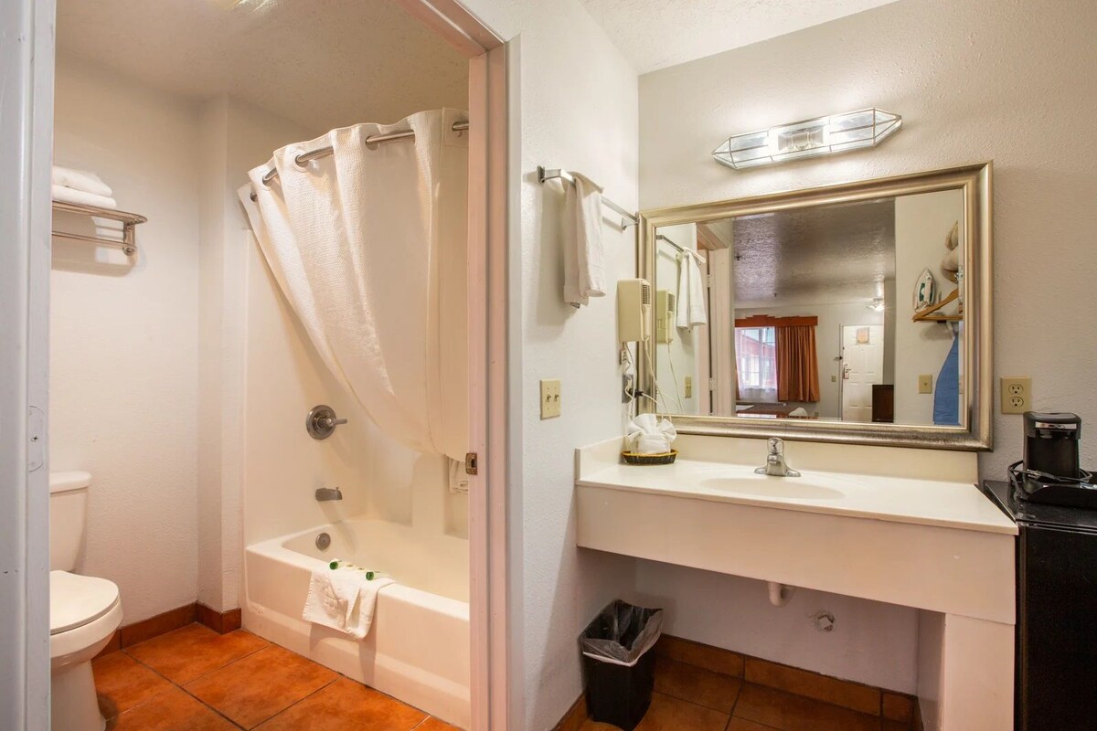 A bathroom with a bathtub, a sink, a mirror, and a trash bin.