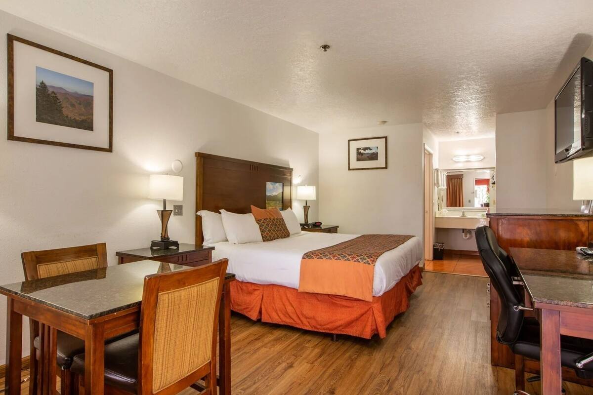 A hotel room with a bed, a desk, a chair, a TV, and a bathroom visible in the background.