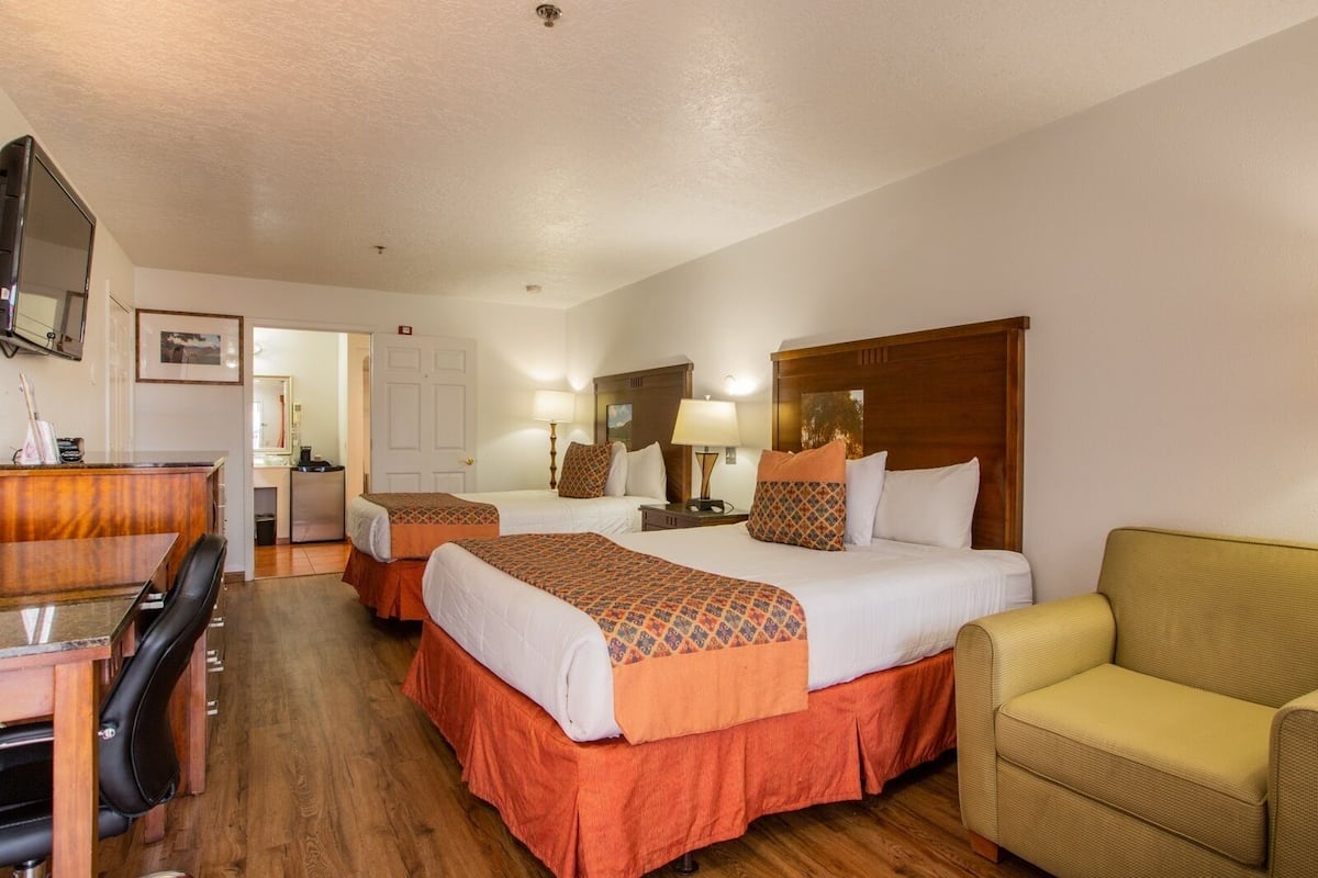 A hotel room with two beds, a desk, a chair, a television, and a couch.