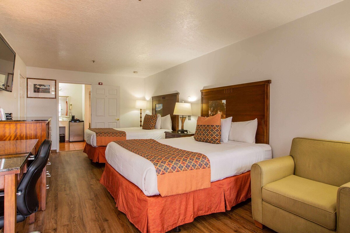A hotel room with two beds, a desk, a chair, and a sofa.