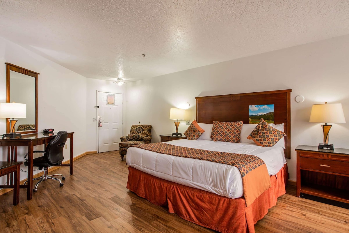 A hotel room with a large bed, a desk, a chair, a nightstand, and a lamp.