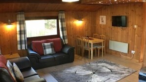 Hyggelig træindretning med sofa, spisebord og fjernsyn ophængt på væggen.