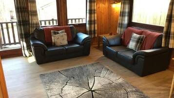 A cozy living room with two dark leather sofas, a wooden coffee table, and a large wooden floor rug.