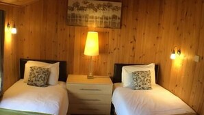 Et værelse i en træhytte med to senge, et natbord med en lampe og vægmonteret belysning.