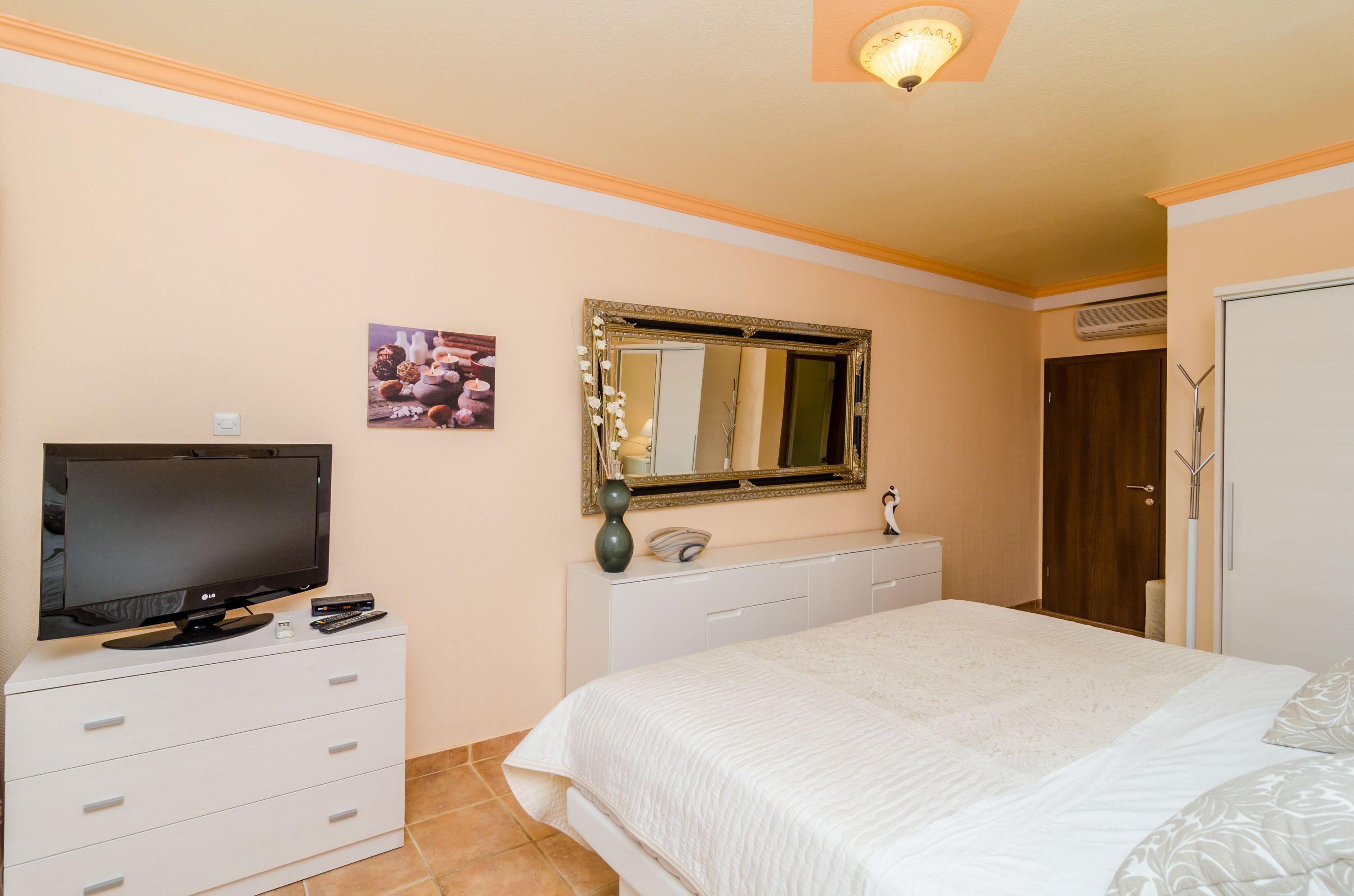 A bedroom with a bed, a television, a dresser, a mirror, and a door.