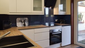 Une cuisine compacte avec des meubles blancs, une hotte noire, un four encastré et un four à micro-ondes.