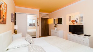 Una camera d'albergo con un letto, una TV, un comò e una porta che conduce a un'altra stanza.