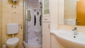 Un baño moderno con ducha de vidrio, inodoro blanco y lavamanos con espejo.
