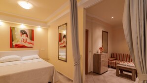 Habitación de hotel con cama, sofá, una mesita, espejo y un cuadro en la pared.