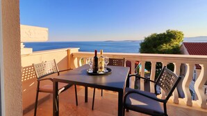 Un balcon avec une table dressée pour deux personnes, une bouteille et des verres, offrant une vue sur la côte.